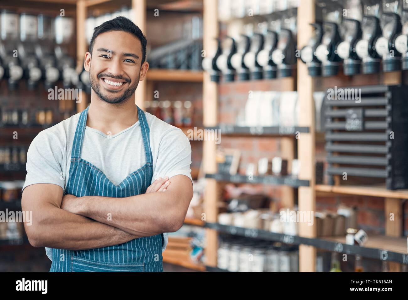 Ritratto di un giovane cameriere ispanico felice in piedi con le braccia incrociate in un negozio o in un bar. Un uomo cordiale e un proprietario di una caffetteria che gestisce un successo Foto Stock