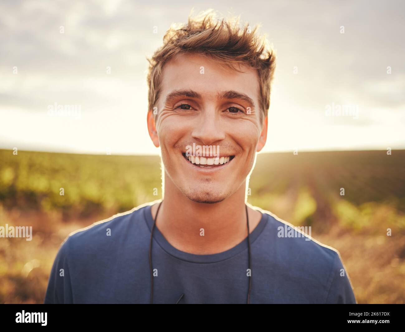 Felice, faccia e natura con un uomo al tramonto, godendo di libertà con un sorriso e stando in piedi su un campo d'erba di giorno. Viaggi, vacanze e mattina Foto Stock