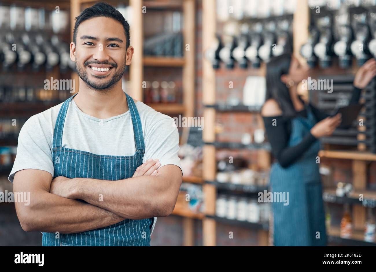 Ritratto di un giovane cameriere ispanico felice in piedi con le braccia incrociate in un negozio o in un bar. Un uomo cordiale e un proprietario di una caffetteria che gestisce un successo Foto Stock
