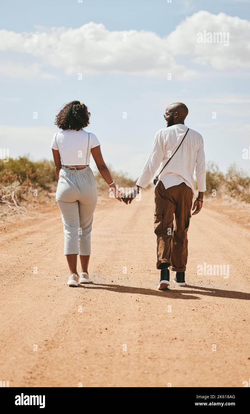 Coppia nera, amore e tenere le mani indietro vista in natura a piedi in vacanza su deserto, sabbia o strada sterrata. Romanticismo, safari e uomo, donna e legame Foto Stock
