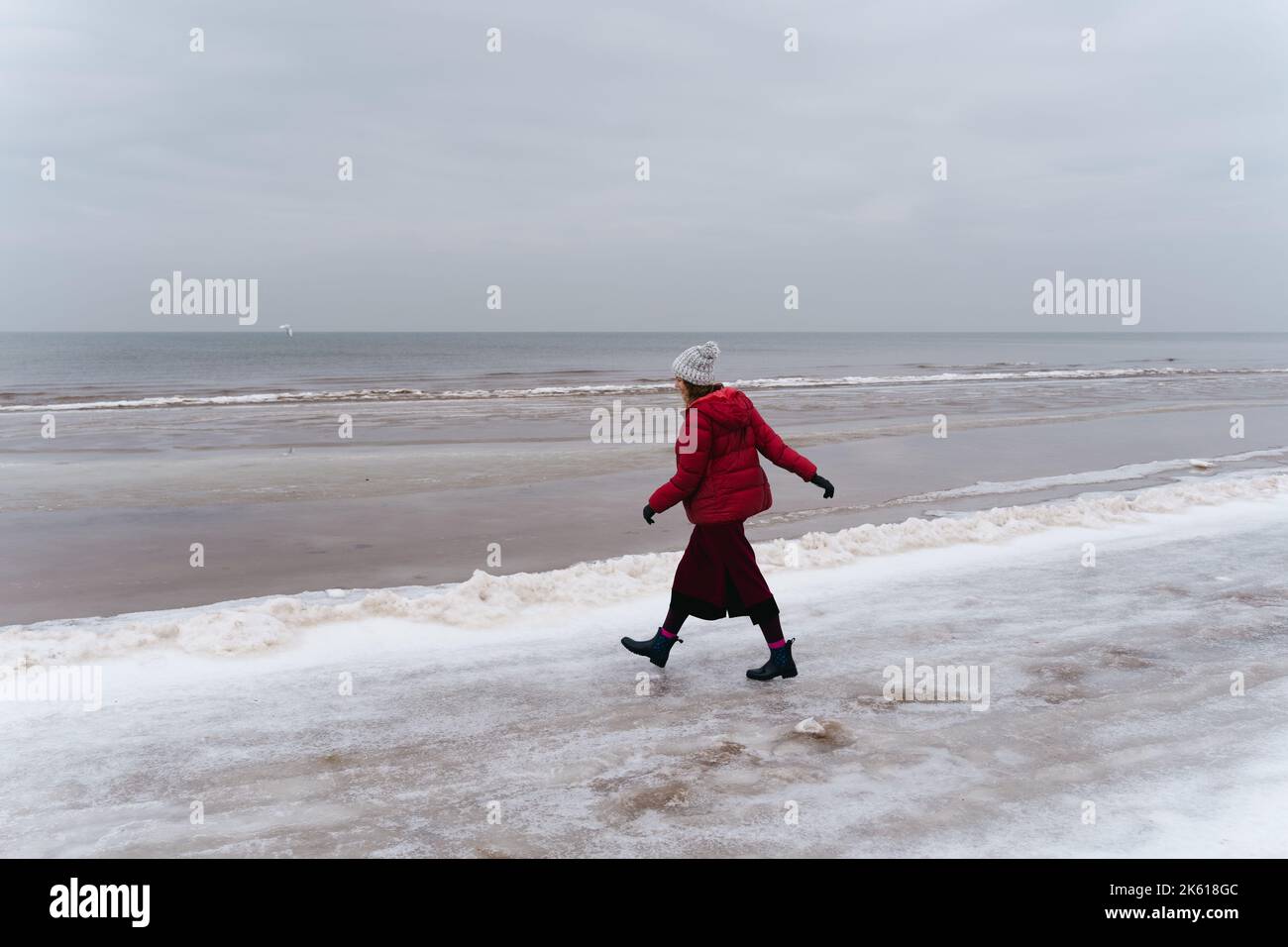 Una donna in rosso cammina in inverno lungo la riva del Mar Baltico a Jūrmala, Lettonia Foto Stock