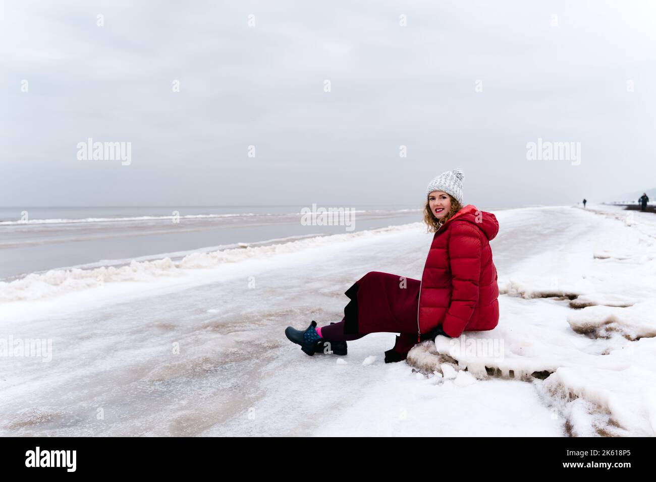 Una donna in abiti caldi d'inverno riposa seduta sulla spiaggia di Jūrmala, in Lettonia Foto Stock