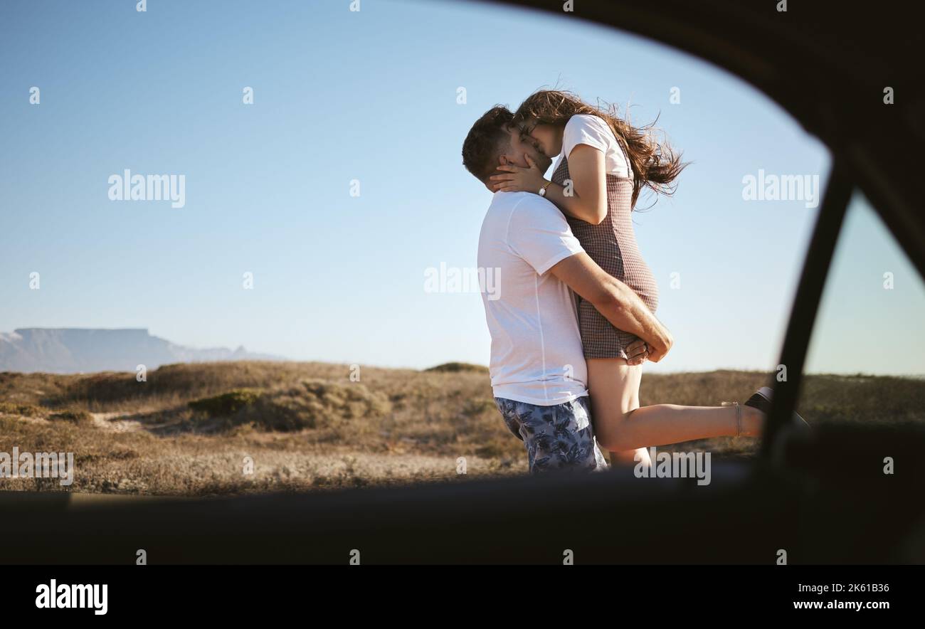 Bacia, amore e coppia in viaggio con auto nella natura della California insieme durante l'estate. Giovane uomo e donna che baciano mentre in vacanza con Foto Stock