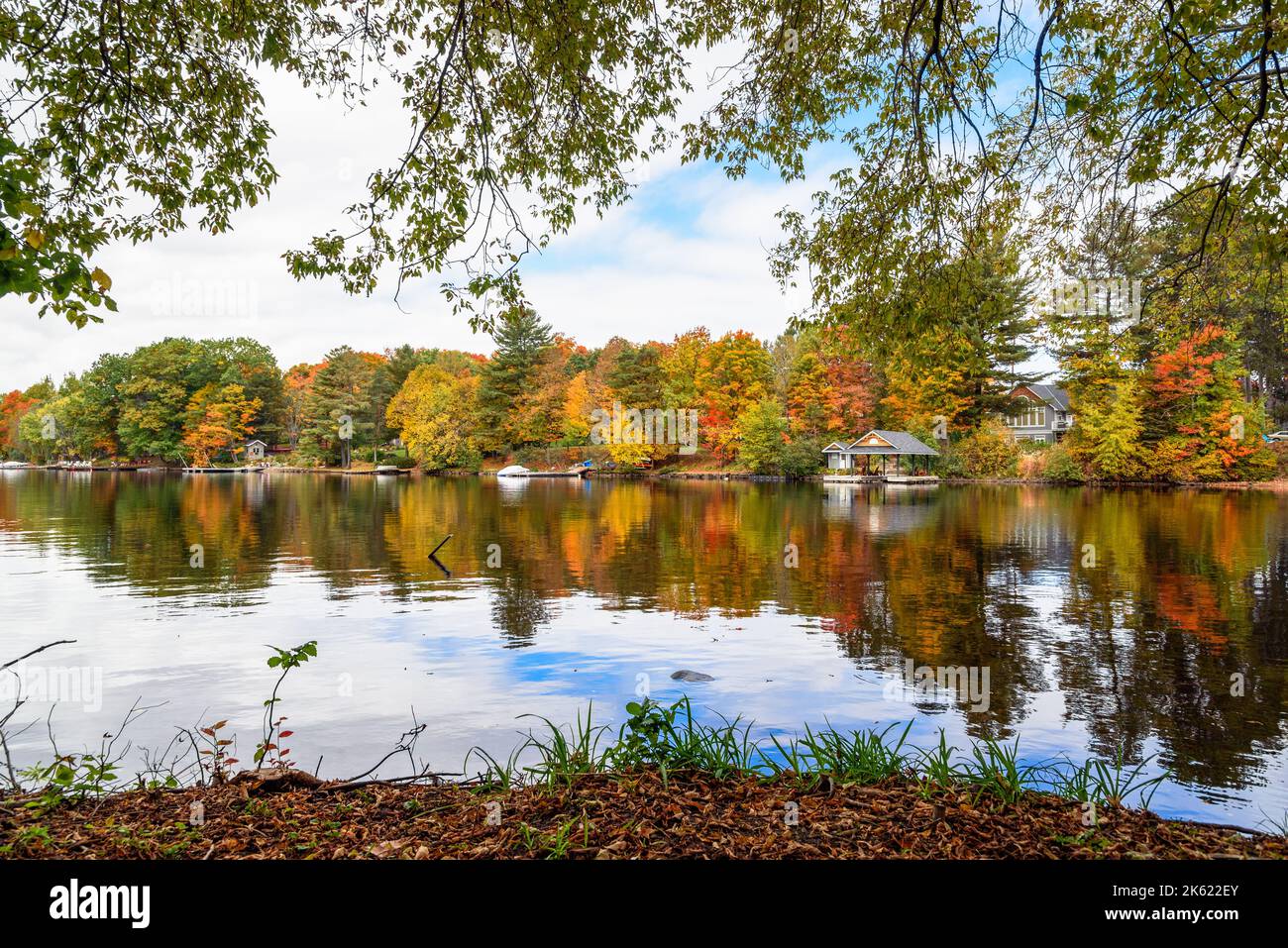 Pontili in legno lungo una riva boschiva di un fiume in una nuvolosa giornata autunnale. Splendidi colori autunnali e riflessi in acqua. Foto Stock