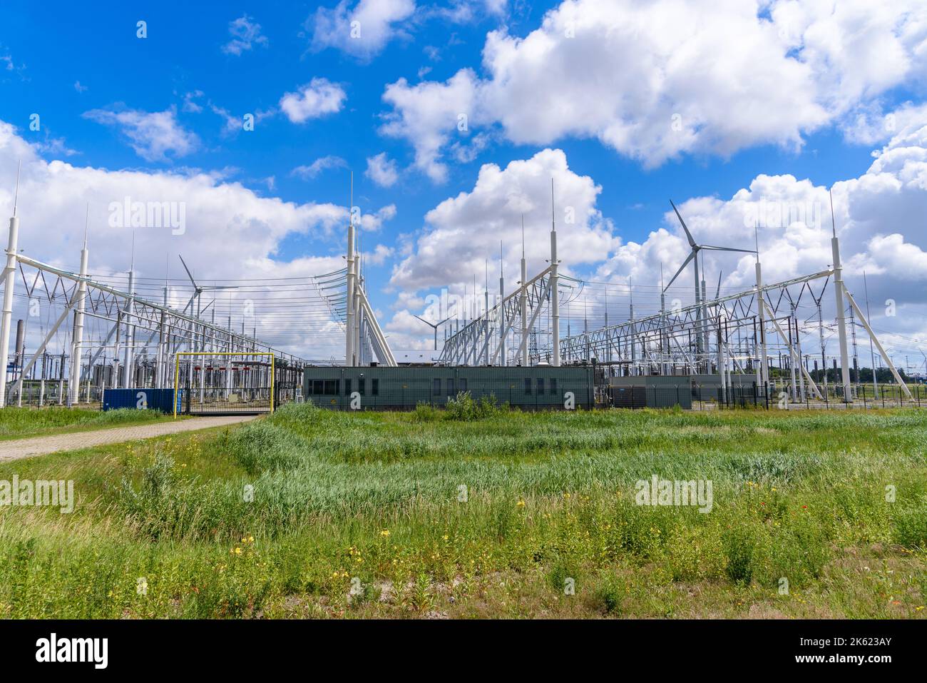 Sottostazione elettrica in campagna sotto il cielo blu con le nuvole in una giornata di sole estate. Le turbine eoliche sono in background. Foto Stock
