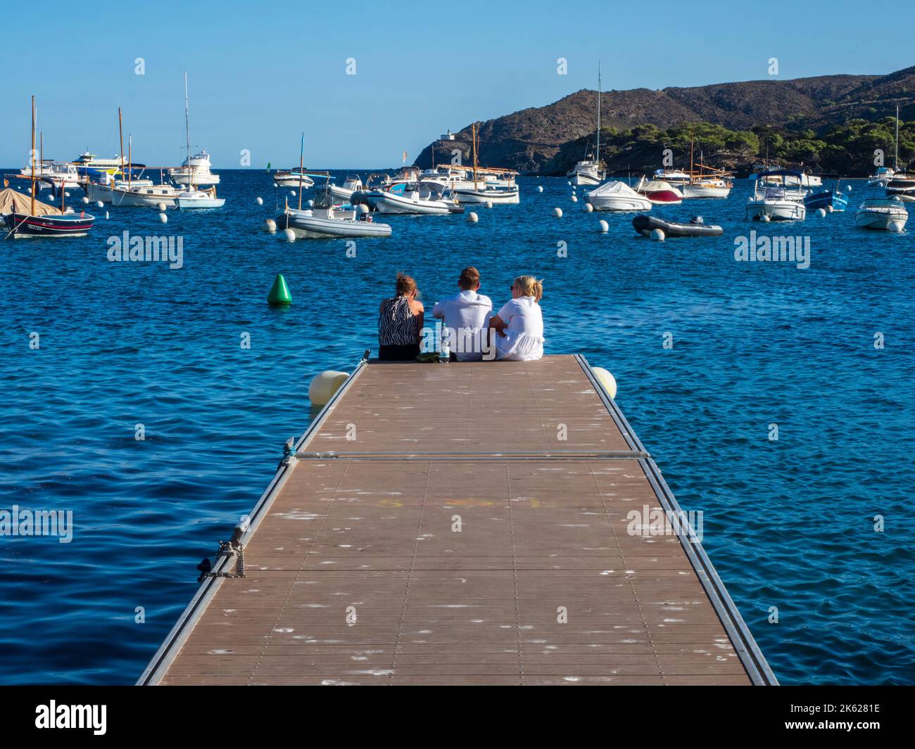 Gruppo di giovani turisti seduti alla fine di un molo di pesca nella città di Cadaqués, Girona, Spagna. Foto Stock