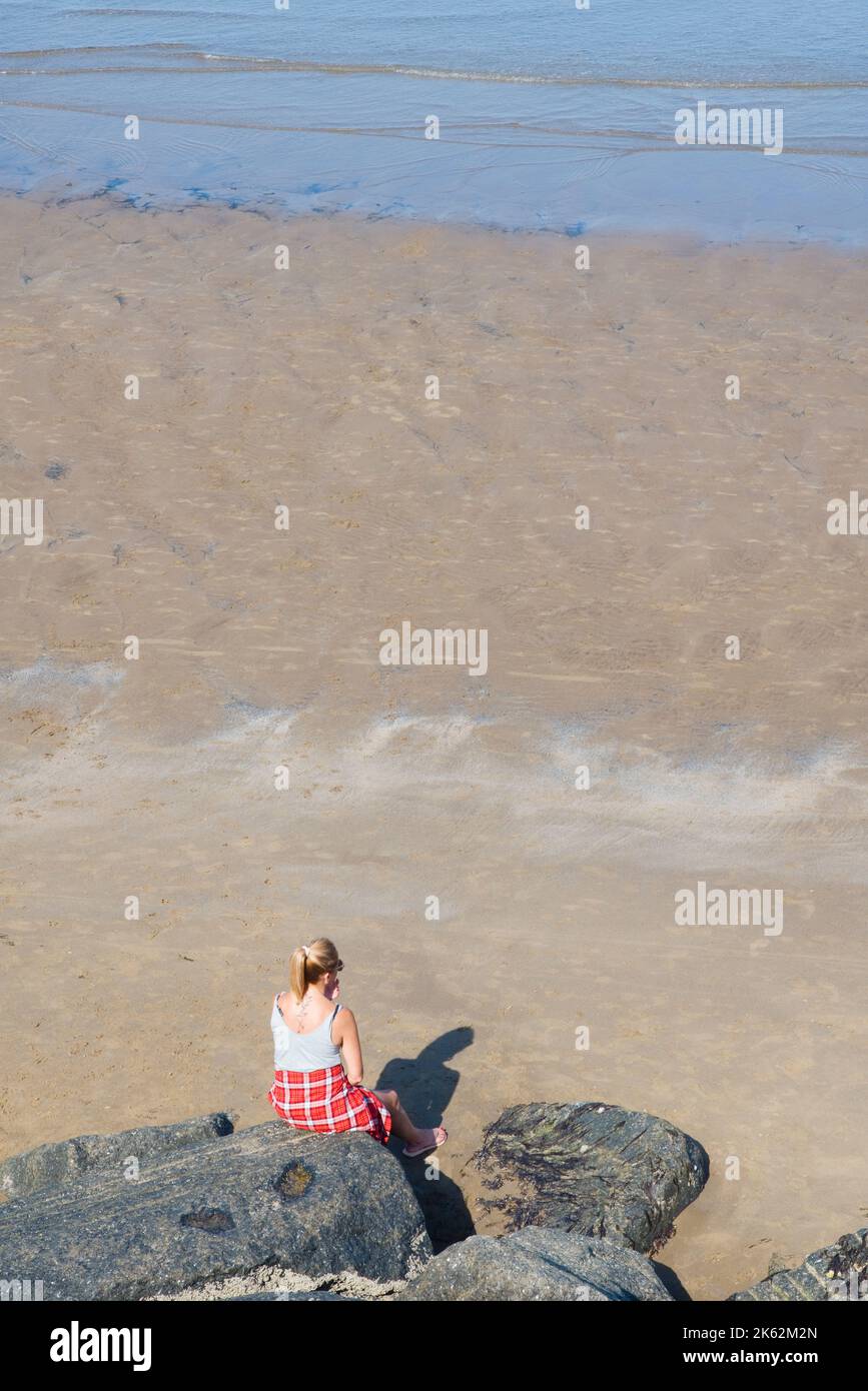 Una donna sola seduta su una roccia che guarda al mare a North Bay, Scarborough Foto Stock