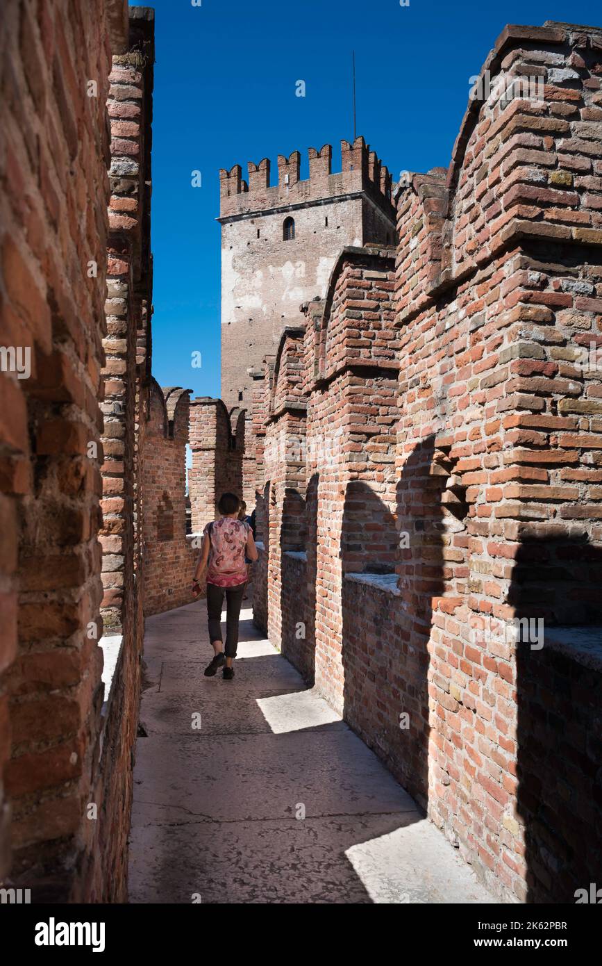 Mura medievali del castello della città, vista in estate di un turista su un passaggio pedonale esplorando i merli distintivi coda di rondine del Castelvecchio, Verona Foto Stock