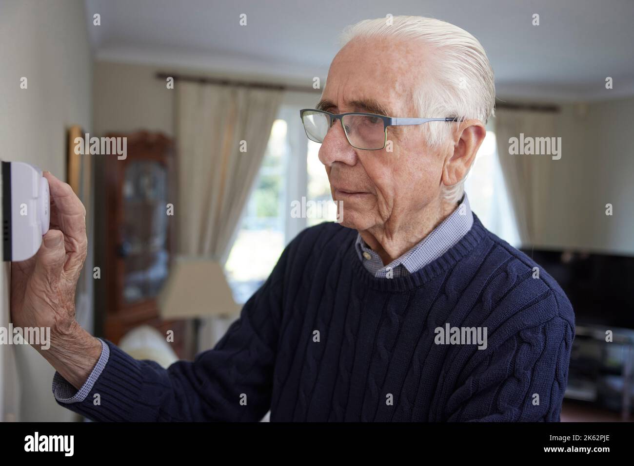 Uomo anziano preoccupato per la riduzione del termostato centrale di riscaldamento a casa in crisi energetica Foto Stock