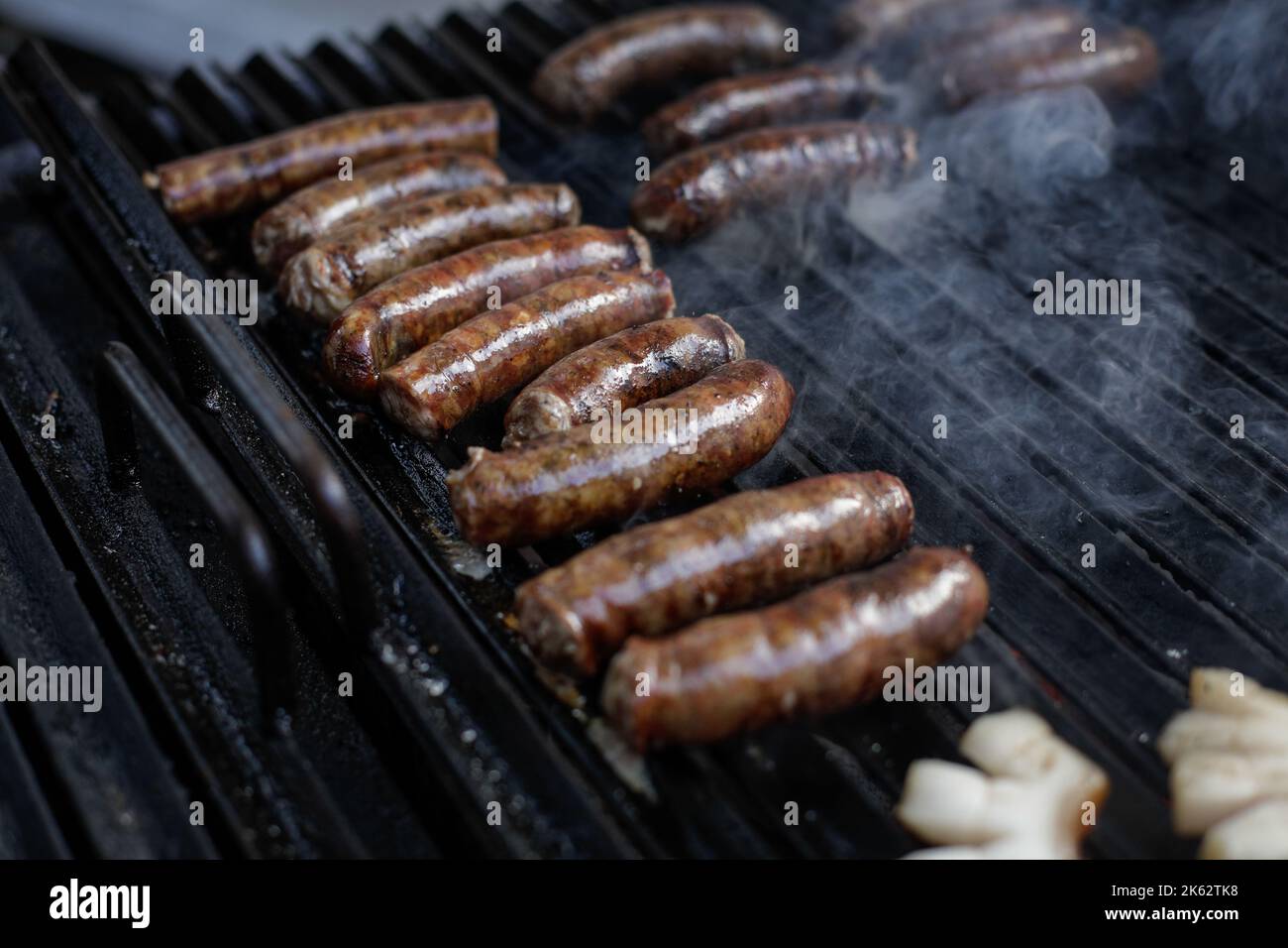 Profondità di campo poco profonda (focus selettivo) dettagli con salsicce di maiale cucina su una griglia barbecue, in un mercato agricolo europeo. Foto Stock