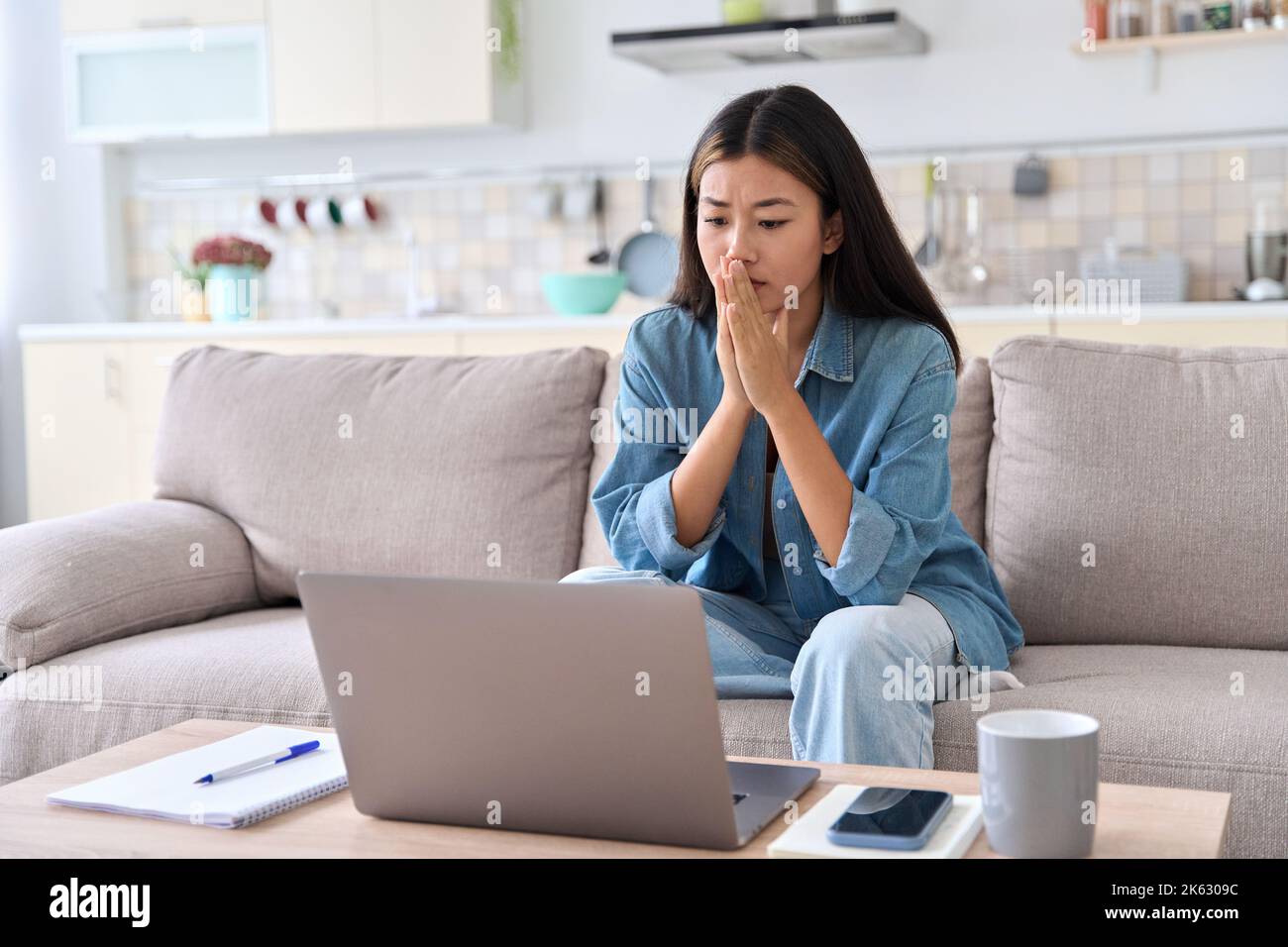 Nervosa donna asiatica che guarda lo schermo del notebook preoccupandosi delle cattive notizie Foto Stock