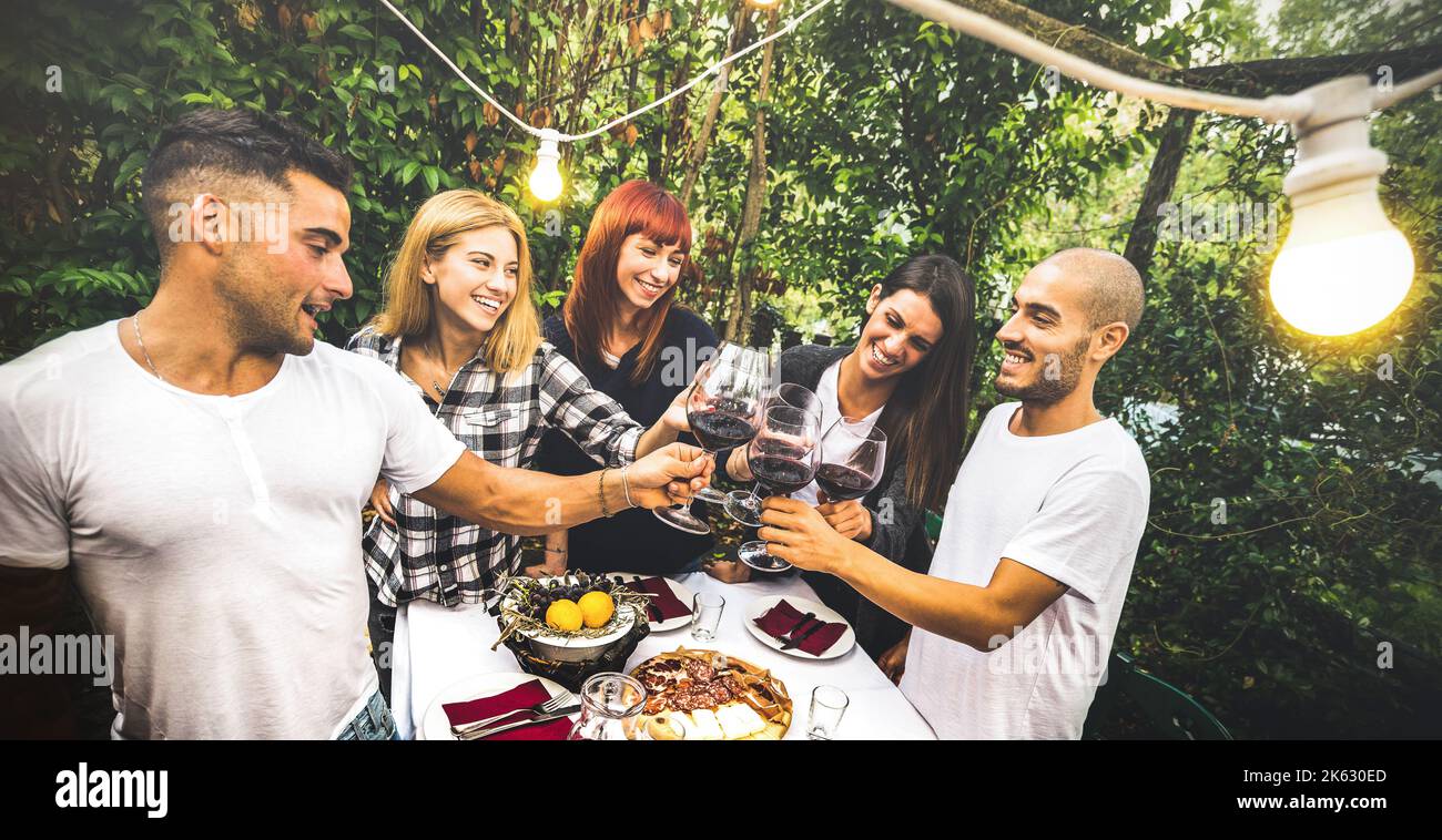 Amici felici che si divertono a bere vino rosso nel cortile giardino festa - giovani amicizia concetto insieme a casa fattoria vigneto cantina - Focus sul backg Foto Stock