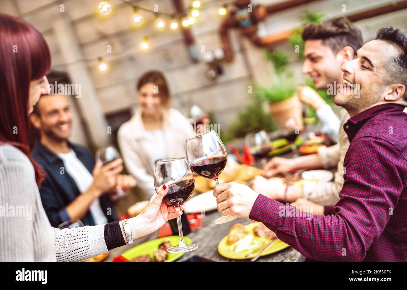 Amici felici che si divertono a bere vino rosso sul balcone durante la cena privata - giovani che mangiano insieme cibo barbecue al ristorante di moda - Dining l Foto Stock