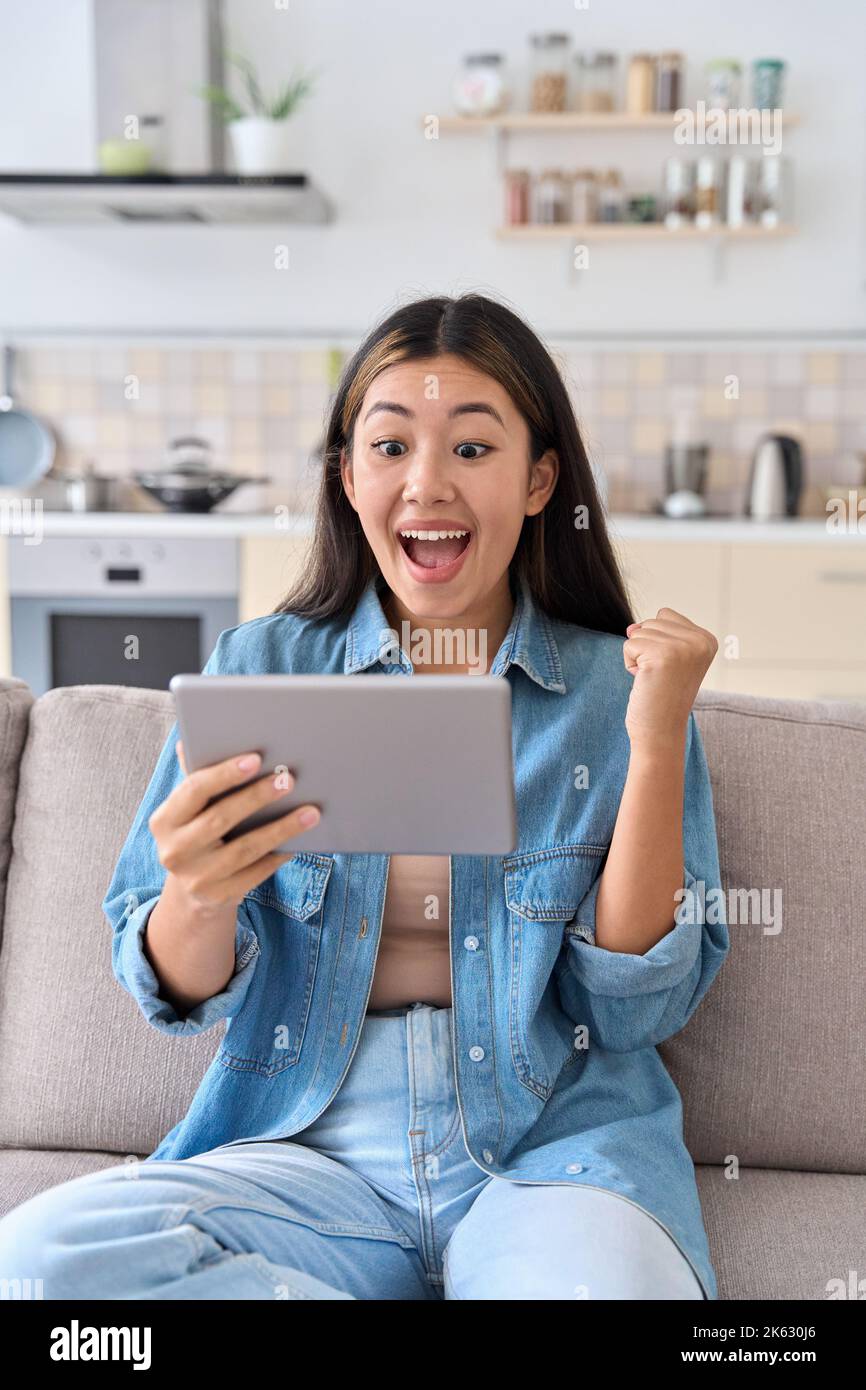 Donna asiatica entusiasta che festeggia il successo guardando lo schermo del tablet digitale Foto Stock