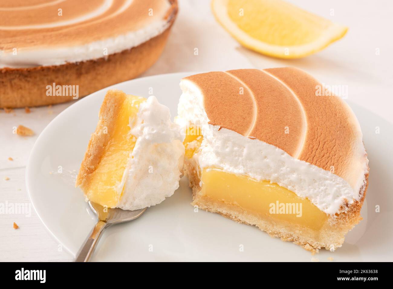 Primo piano di una porzione di crostata di limone con il condimento meringa sul piatto bianco con il boccaglio su una forchetta. Foto Stock