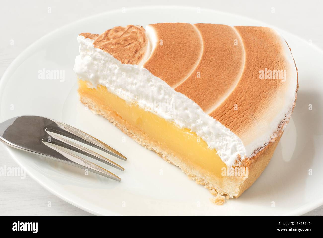 Un pezzo di crostata di limone con guarnizione meringa su un piatto bianco accanto a una forchetta. Foto Stock