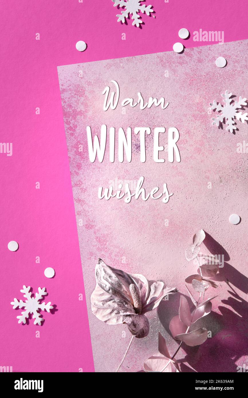 Messaggio di saluto caldo auguri invernali. Giacitura astratta con fiore di giglio di cala secco e ramoscello di eucalipto dipinto di rosa metallizzato. Neve fiocchi di carta inverno su Foto Stock