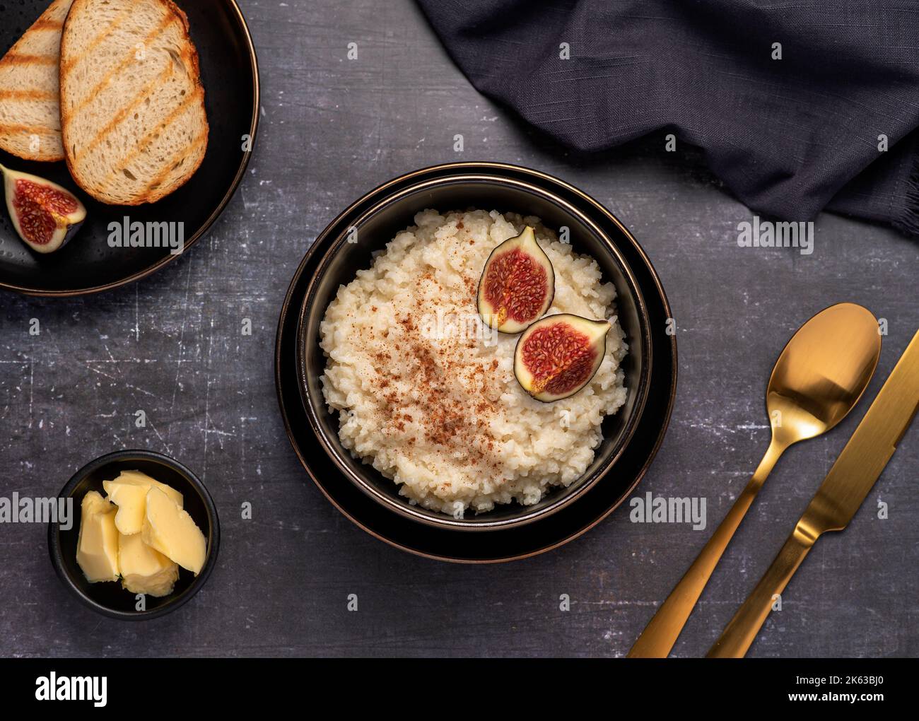 Fotografia alimentare di porridge di riso, budino, cereali, fichi, cannella, burro, pane tostato Foto Stock