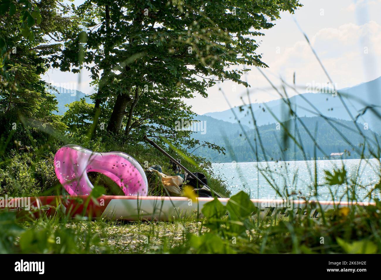 Walchensee. Punto da bagno con cuore rosa, pannello di SUP, bottiglie di birra, utensili da bagno. Vista sulla West Shore e sulle montagne. Foto Stock