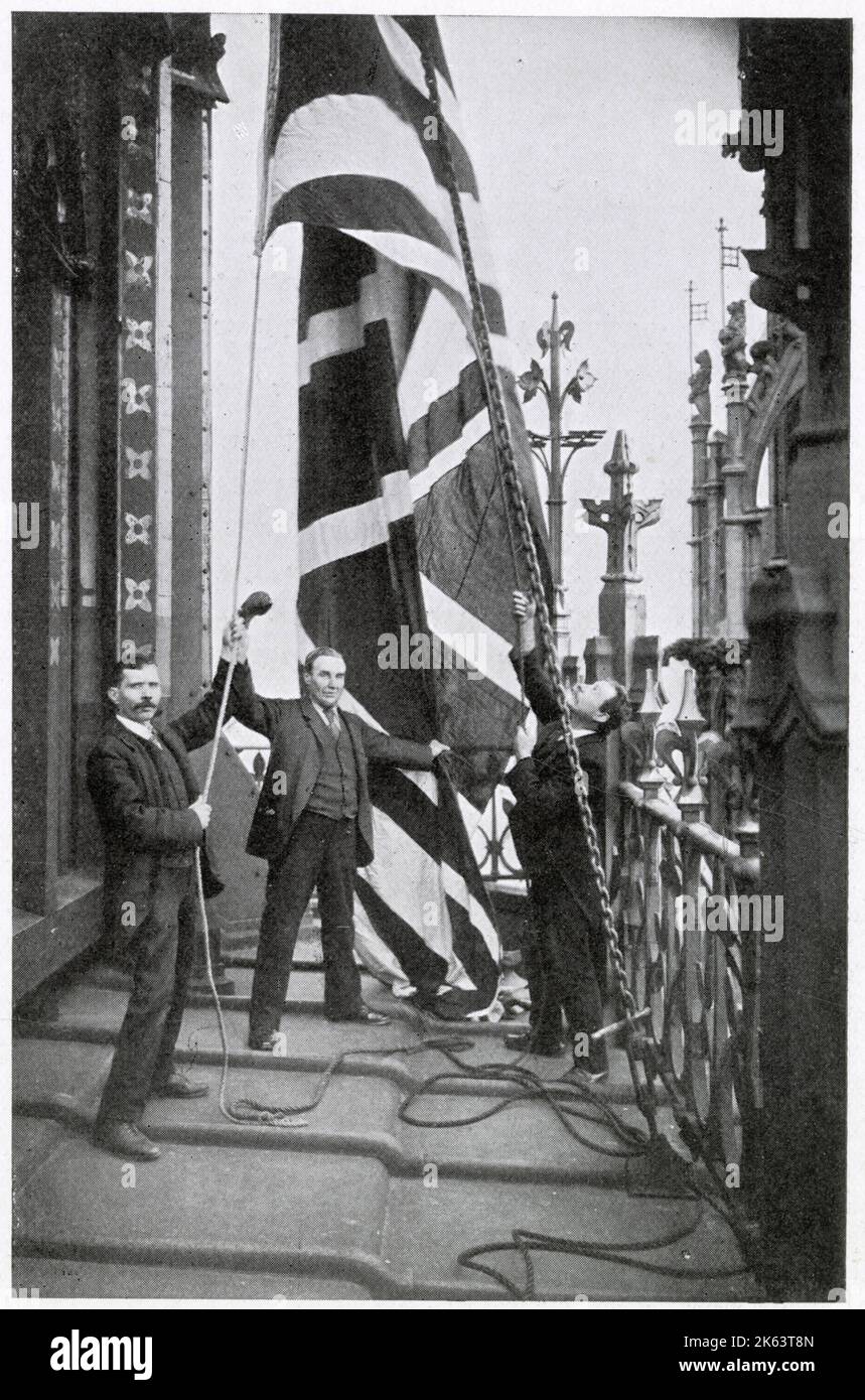 Quando il sovrano si trova nell'edificio del Parlamento, il Royal Standard è volato, sulla Victoria Tower. Fotografia che mostra due uomini che issano la bandiera Union Jack. Foto Stock