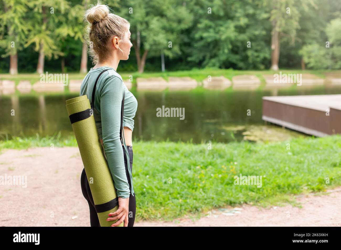 una donna snella nel parco in estate, con un tappetino verde da palestra dietro la schiena Foto Stock