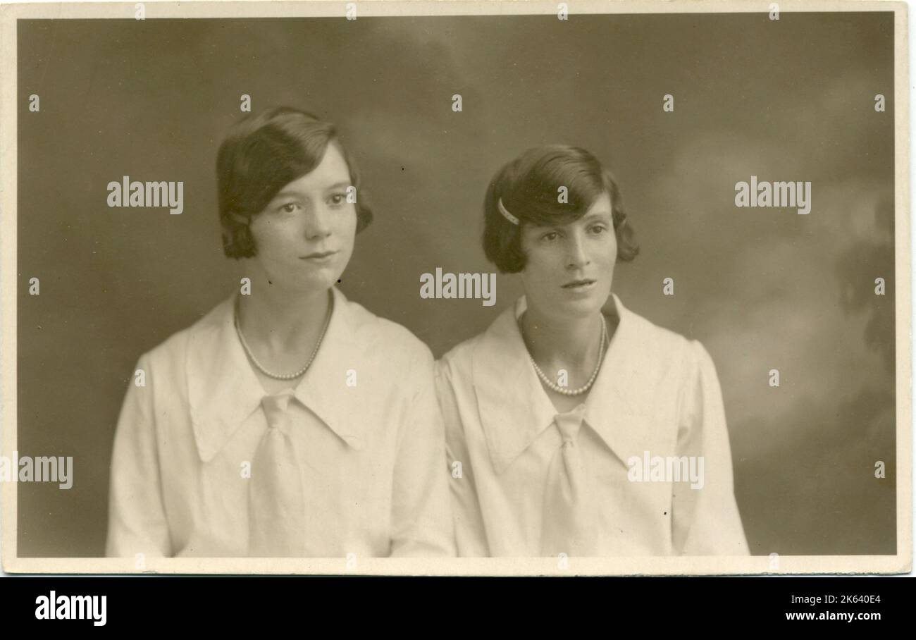 Ritratto in studio di due donne, entrambe con i capelli scuri a fascia e con camicette identiche con colletti grandi e cravatta. Foto Stock