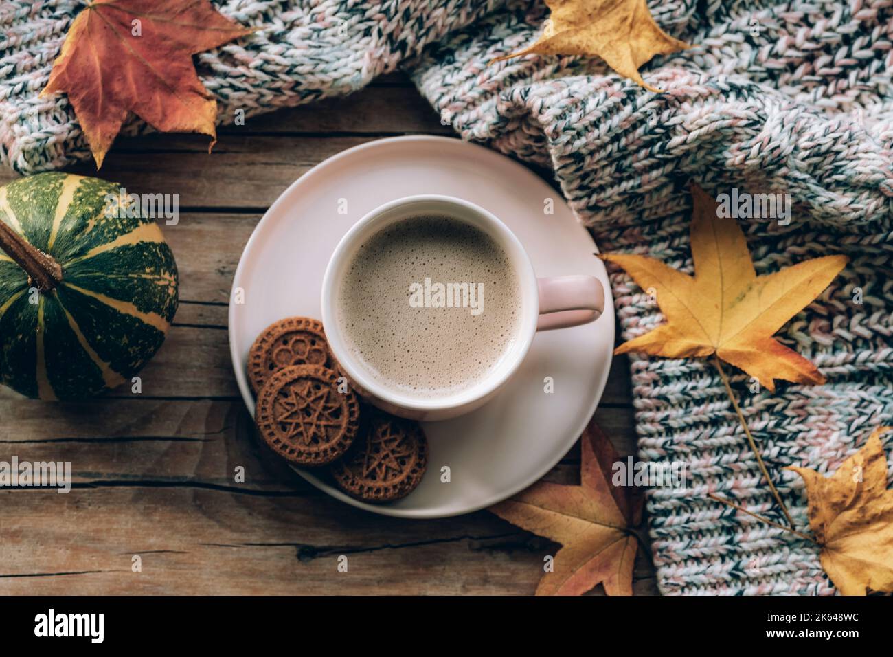 Tazza da caffè con biscotti, zucca, foglie autunnali e maglione a maglia su tavolo di legno. Concetto autunnale. Vista dall'alto, disposizione piatta Foto Stock