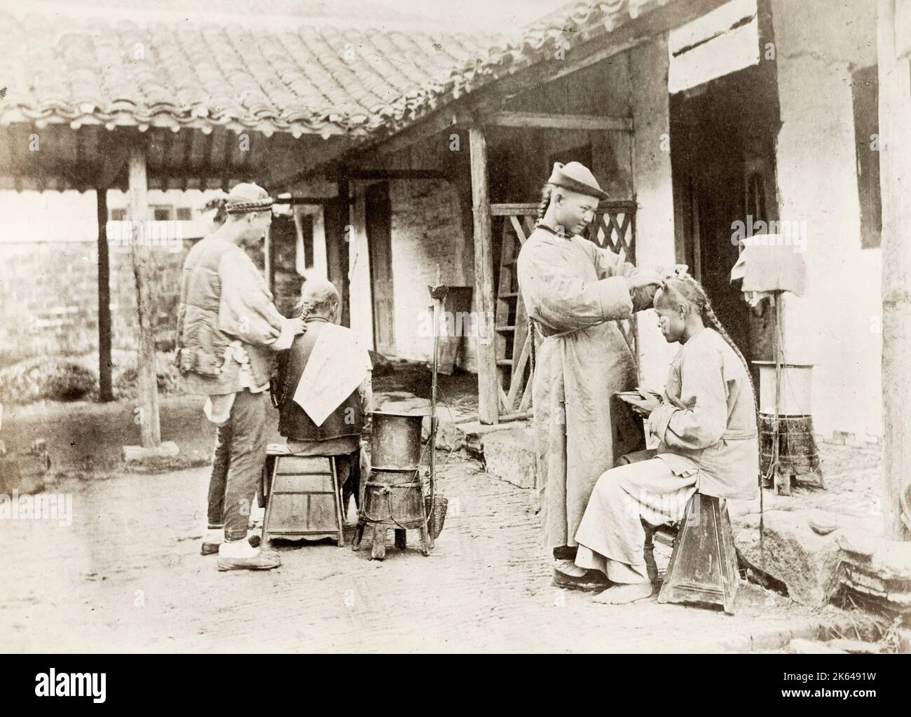 Vintage 19 ° secolo Fotografia: Cina c.1880's - barili itineranti che lavorano su clienti all'aperto, uomini con lunga coda di cue, acconciature ponytail. Foto Stock