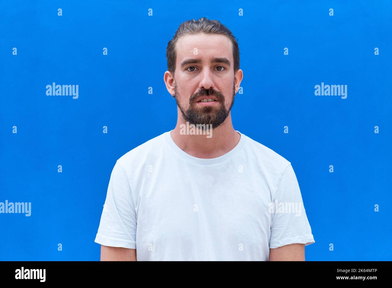 Uomo giovane e bello che indossa una t-shirt casual in piedi su un isolato sfondo blu con un'espressione seria sul viso. Foto Stock