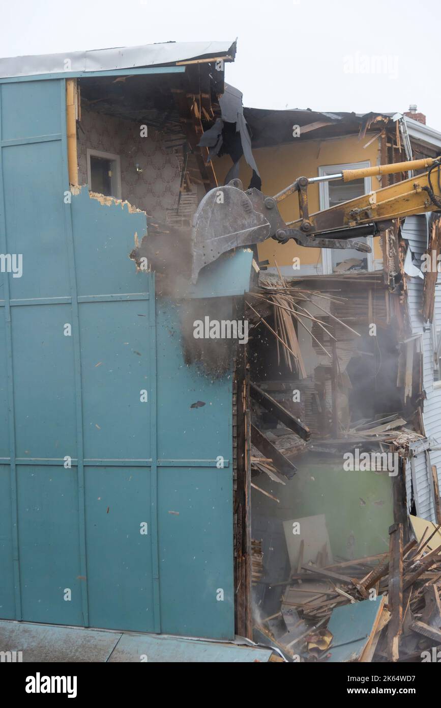 Demolizione di un edificio con un grande retroescavatore. Giornata di Overcast. L'aria è polverosa e sono presenti detriti dalla demolizione. Foto Stock