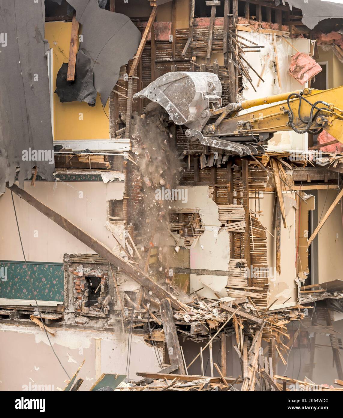 Demolizione di un edificio con un grande retroescavatore. L'aria è polverosa. Mattoni stanno cadendo dal secchio. Sono visibili stecche da parete, carta da parati, isolamento e altro ancora. Foto Stock
