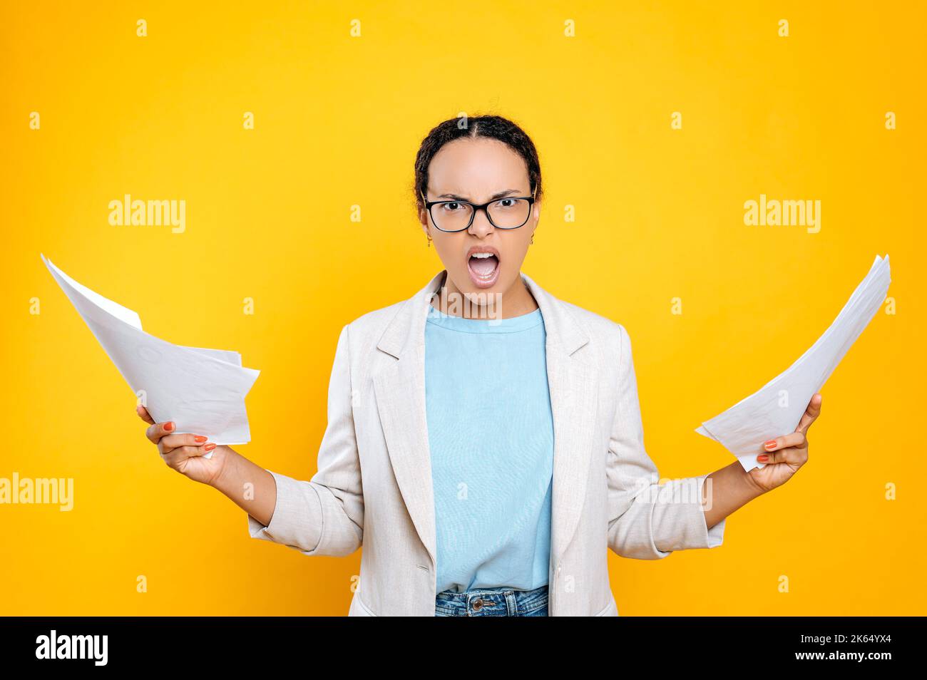 Confuso perplesso preoccupato giovane latino o donna brasiliana, donna d'affari, capo, tenere documenti in mano, tenere la bocca aperta, guardare la macchina fotografica irritata, si trova su sfondo isolato arancione Foto Stock