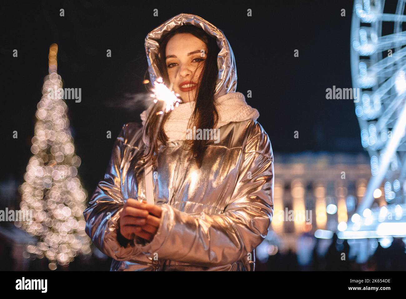 Giovane donna che tiene scintilla mentre si trova in piedi sulla piazza della città durante le vacanze di Natale di notte Foto Stock