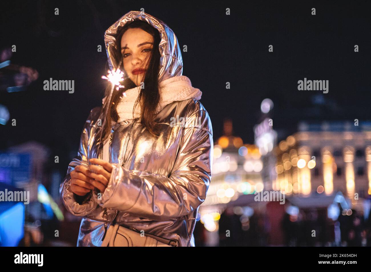 Giovane donna che tiene scintilla mentre si trova in piedi sulla piazza della città durante le vacanze di Natale di notte Foto Stock