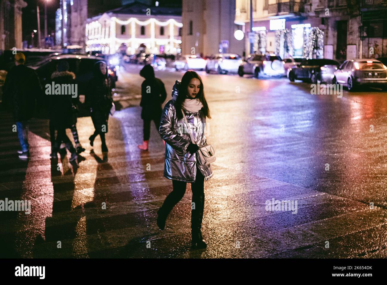 Giovane donna che attraversa la strada in città durante l'inverno di notte Foto Stock