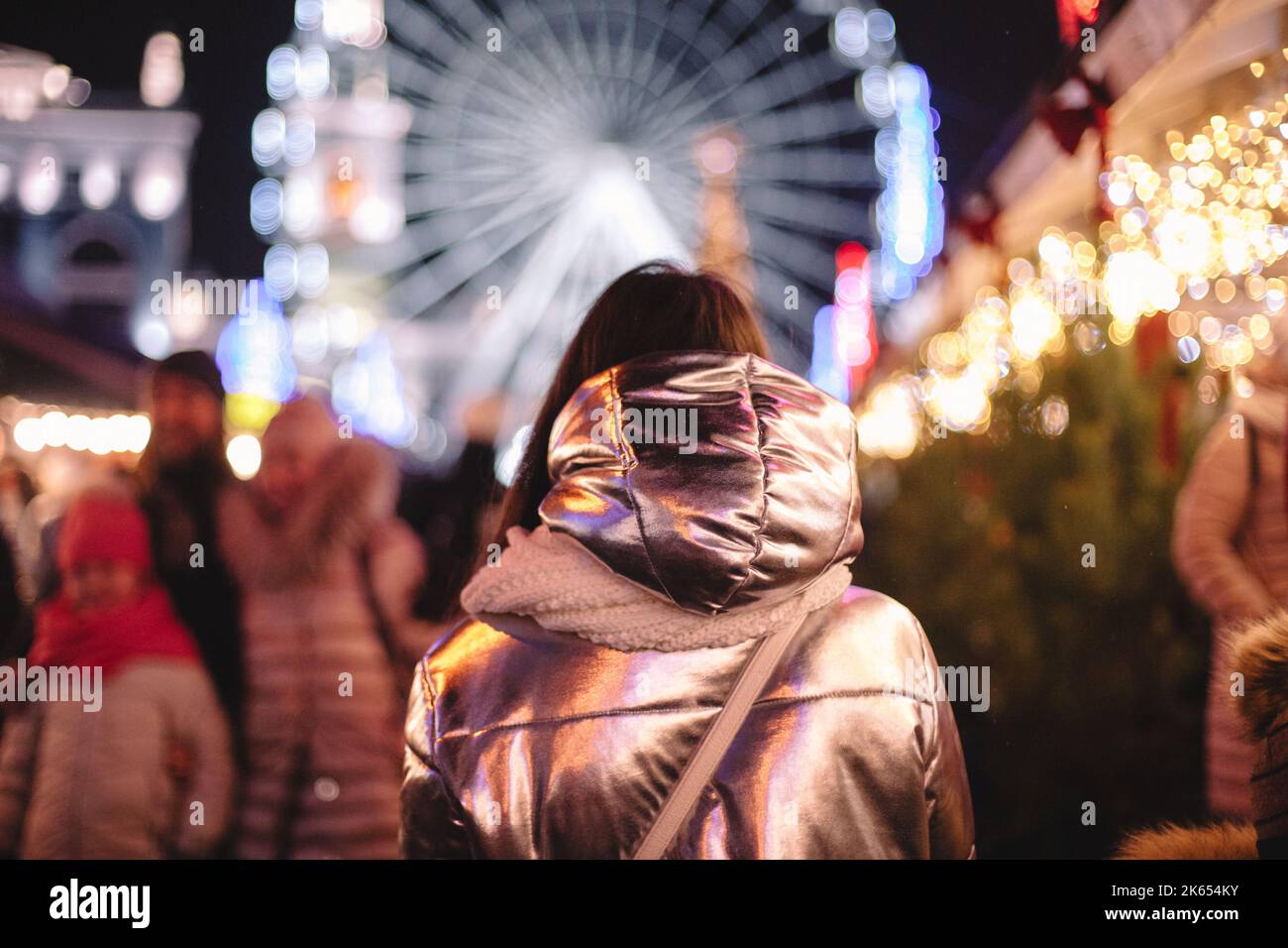 Vista posteriore della giovane donna che cammina nel mercatino di Natale in città di notte Foto Stock