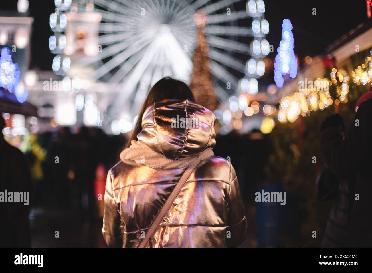 Vista posteriore della giovane donna che cammina nel mercatino di Natale in città di notte Foto Stock