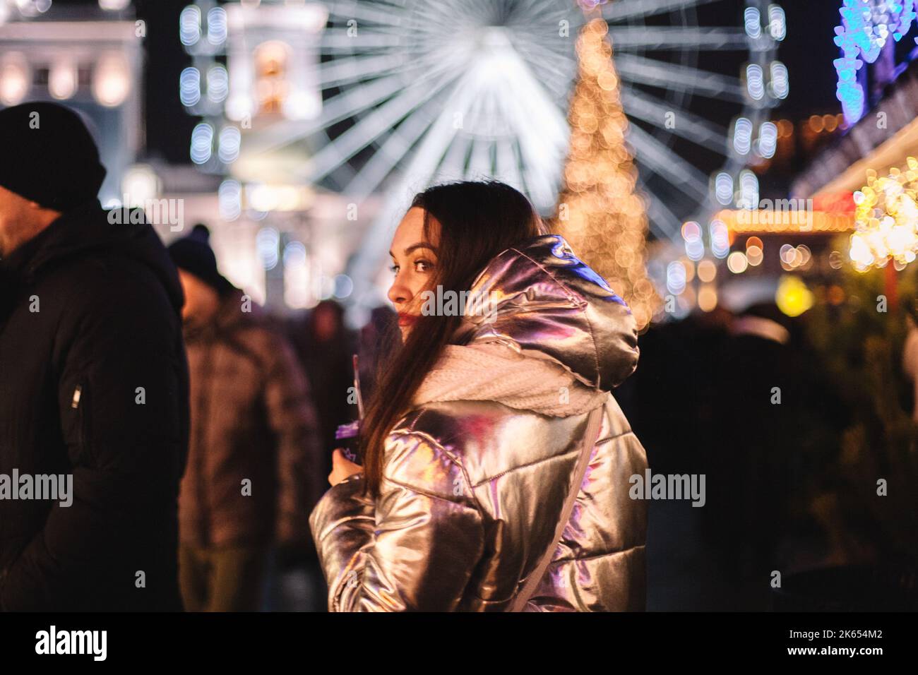 Giovane donna che guarda indietro mentre cammina nel mercato di Natale in città di notte Foto Stock