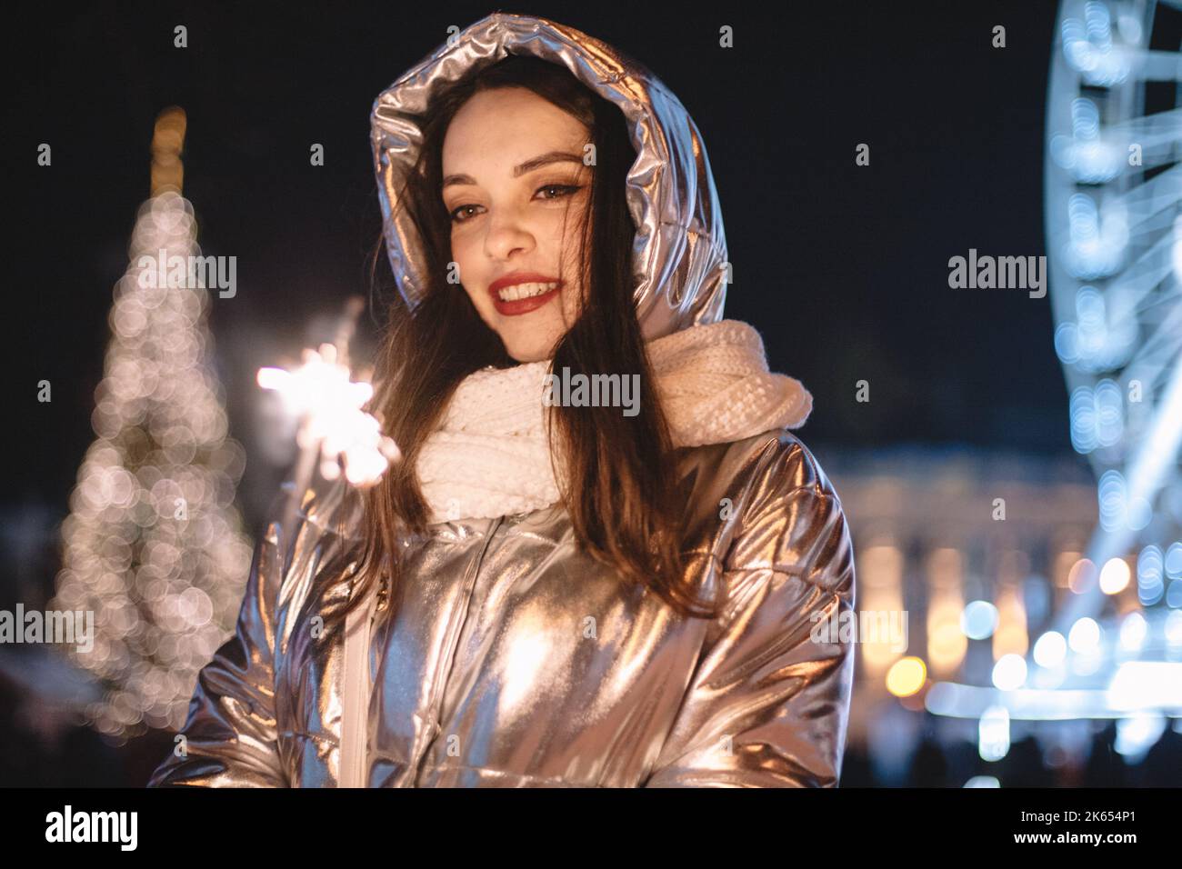 Giovane donna che tiene scintilla mentre si trova in piedi sulla piazza della città durante le vacanze di Natale di notte Foto Stock