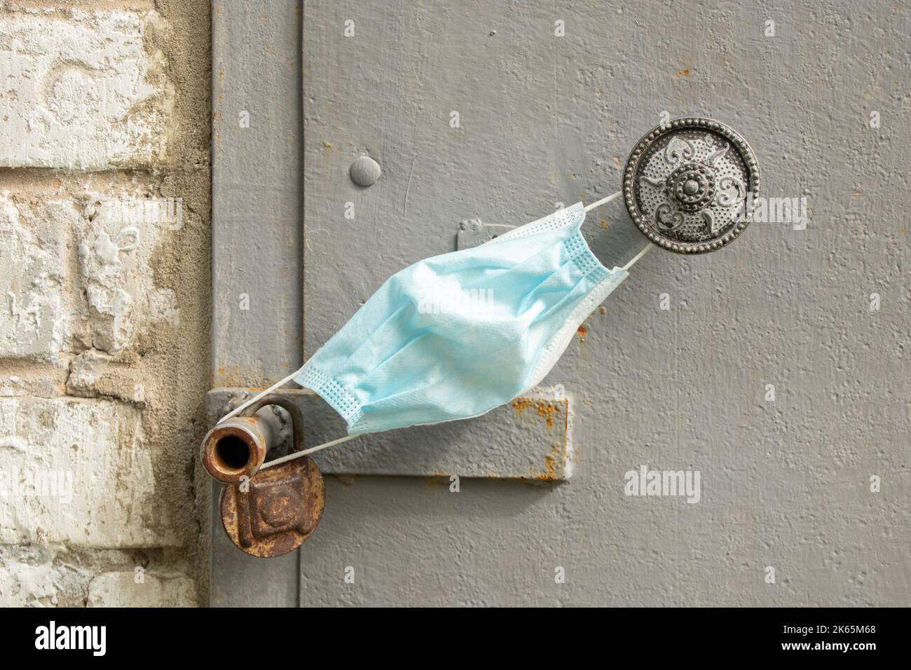 una maschera medica appende sulla maniglia su una vecchia porta arrugginita di ferro sulla strada della casa, fermata in quarantena Foto Stock