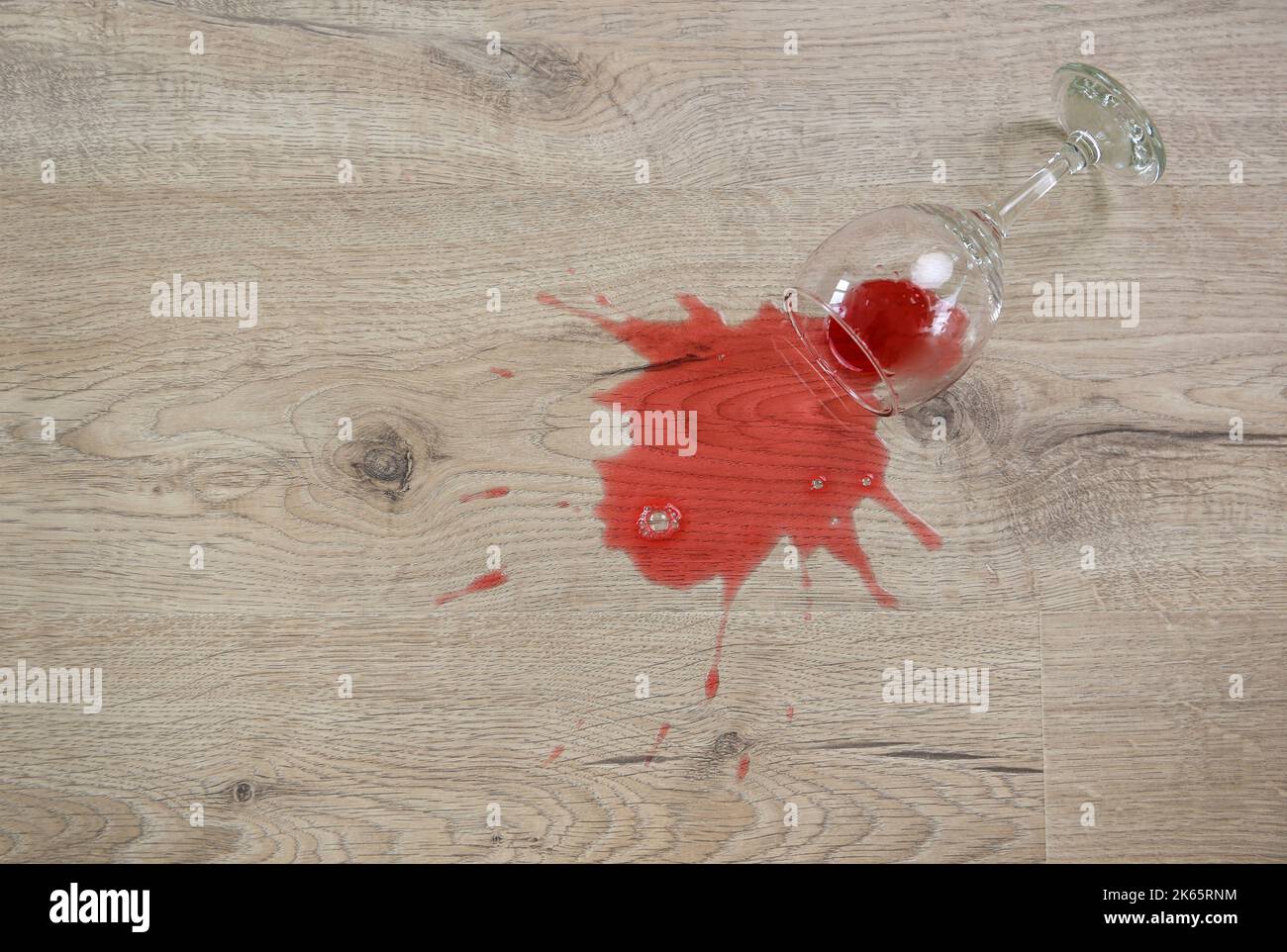 Un bicchiere di vino rosso cadde sul laminato, il vino versato sul pavimento. Foto Stock