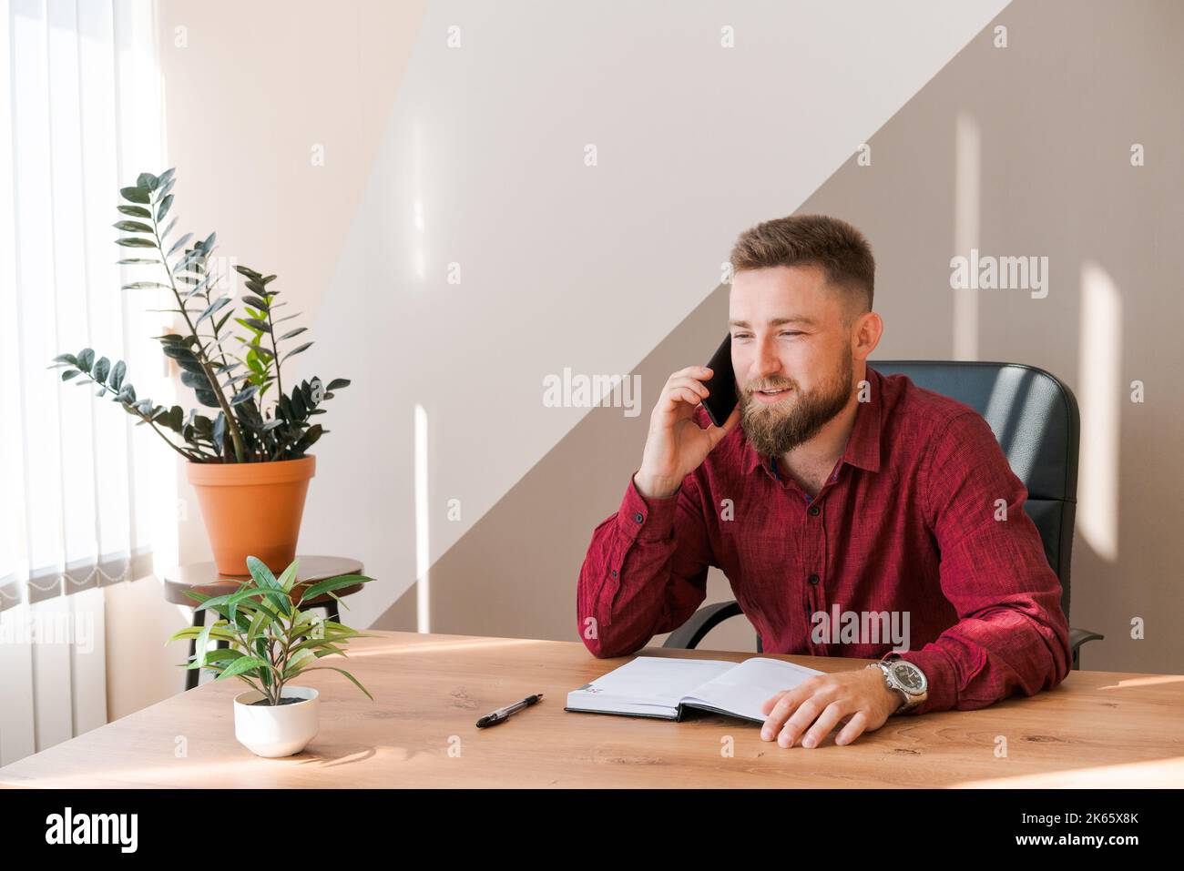 L'uomo affollato di affari sta parlando al telefono e programmi per incontrarsi giornalmente e scrivere un viaggio di affari in un diario sulla scrivania dell'ufficio. Pianificatori di pianificazione del calendario e promemoria del programma. Foto Stock