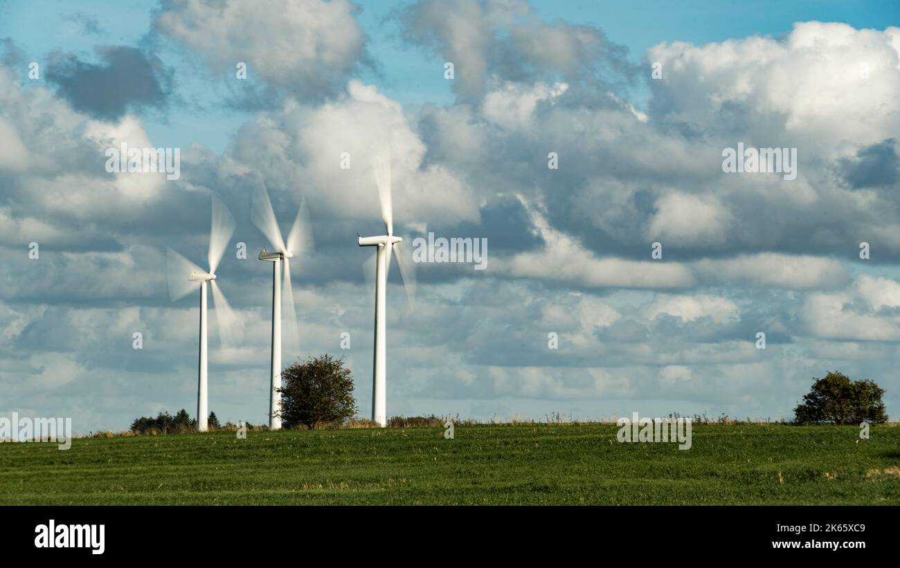 Turbine eoliche su un campo sotto un cielo autunnale soleggiato fotografato con tempo di esposizione e sfocatura del movimento sulle pale del rotore Foto Stock