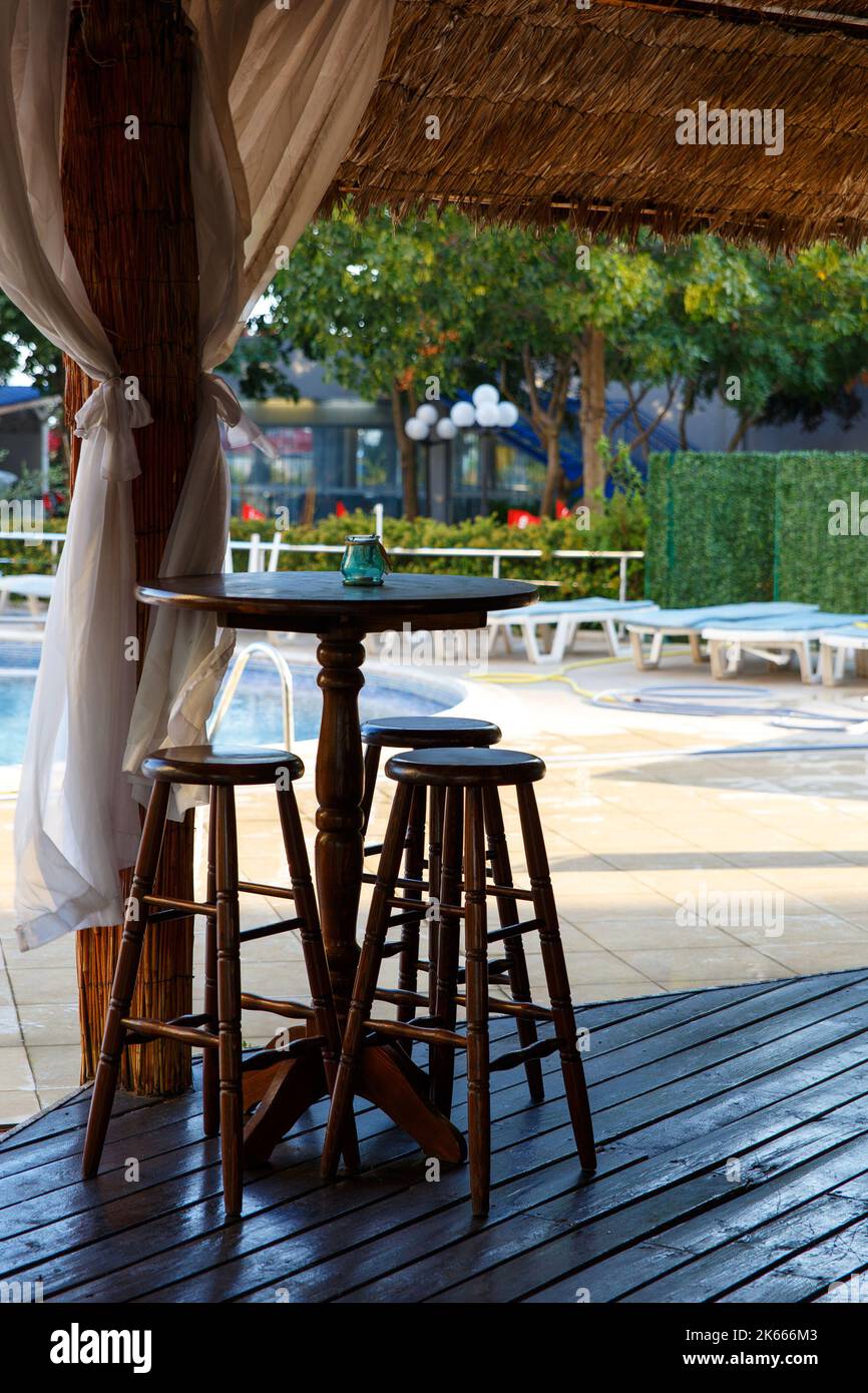 Nessuno si siede allo sgabello di legno al ristorante all'aperto a mezzogiorno vicino ad una piscina. Foto Stock