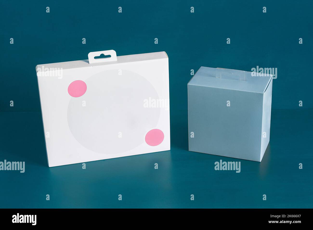 Una scatola di cartone bianca con due cerchi rosa decorativi e una scatola quadrata blu vuota su uno sfondo blu colorato studio con spazio copia. Deposito, specialità gastronomiche Foto Stock