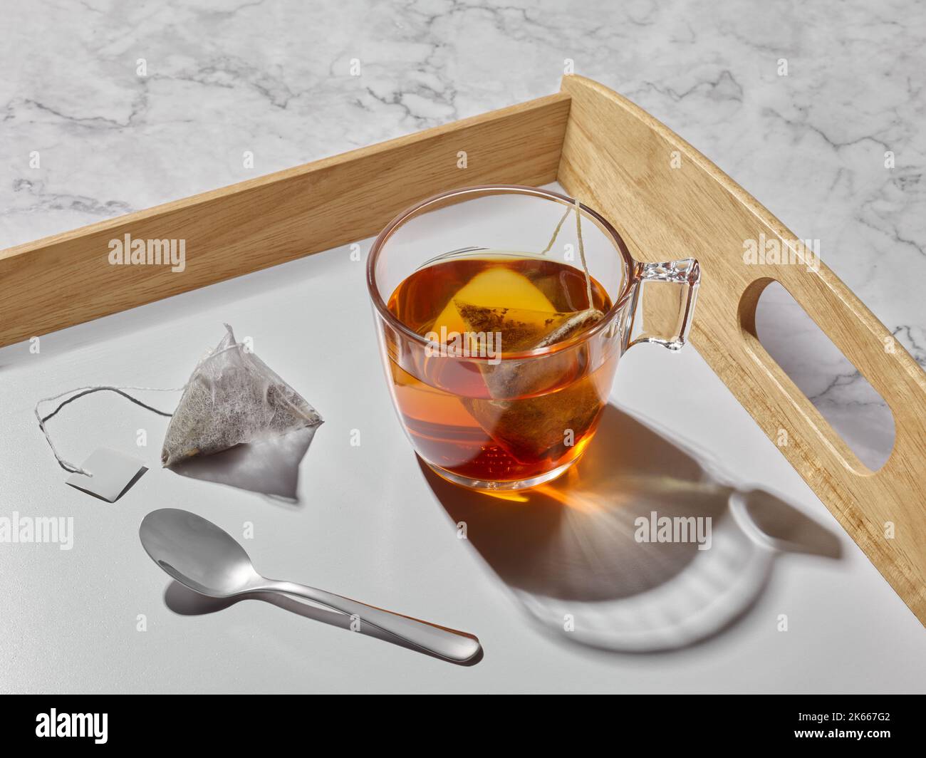 Tazza in vetro con tè, bustina e cucchiaio su un vassoio Foto Stock