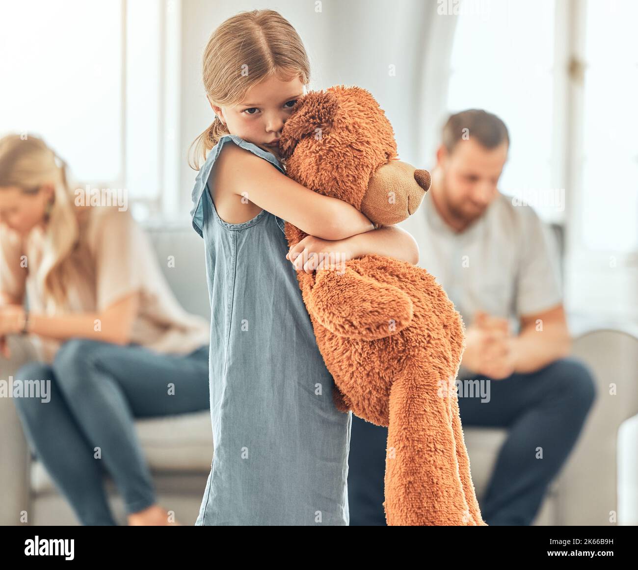 Una ragazza piccola sconvolta che stringe il suo orsacchiotto mentre osserva triste e depresso mentre i suoi genitori discutono sullo sfondo. Pensando ai suoi genitori Foto Stock