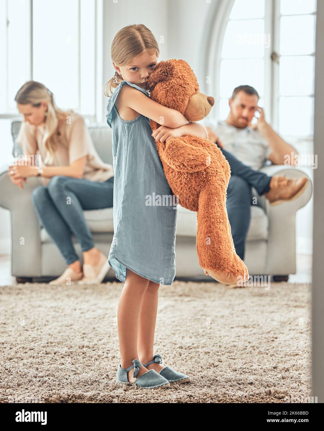 Una ragazza piccola sconvolta che stringe il suo orsacchiotto mentre osserva triste e depresso mentre i suoi genitori discutono sullo sfondo. Pensando ai suoi genitori Foto Stock