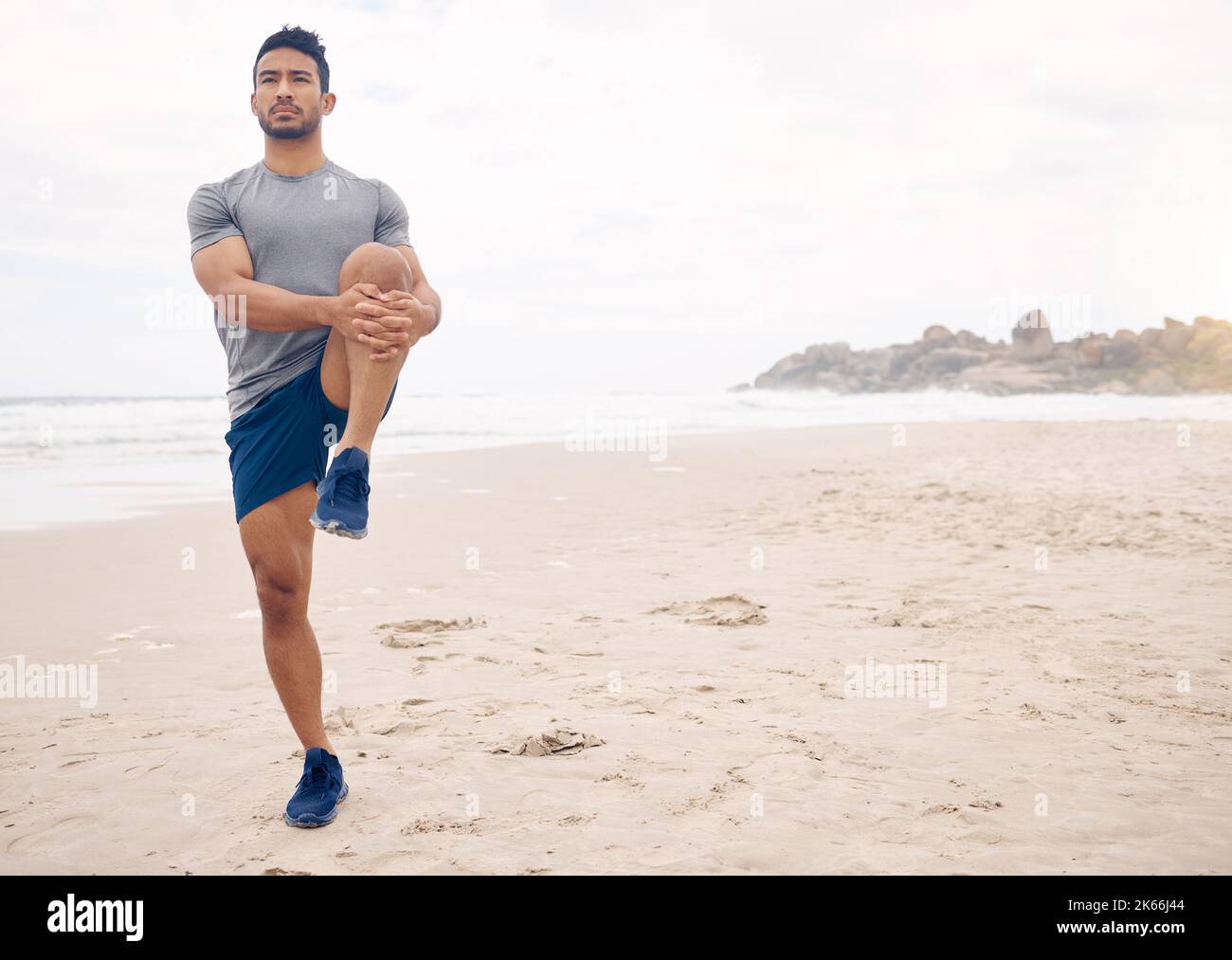 Passare ad un allenamento in spiaggia. Un giovane sportivo che allunga le gambe mentre si esercita in spiaggia. Foto Stock