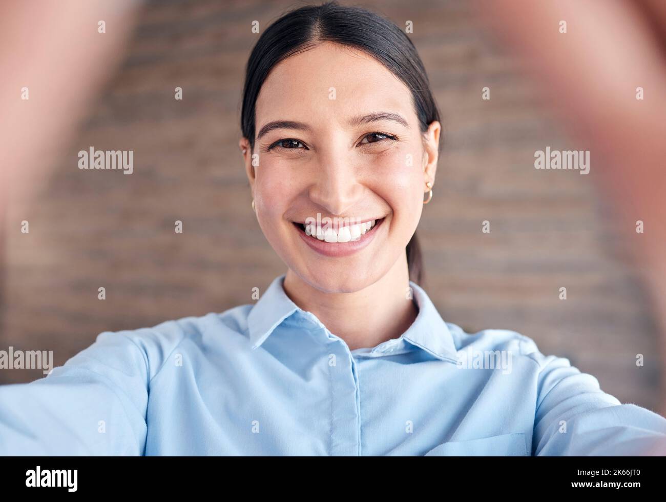 Primo piano ritratto di una giovane donna allegra di razza mista in piedi in un ufficio che prende un selfie Foto Stock
